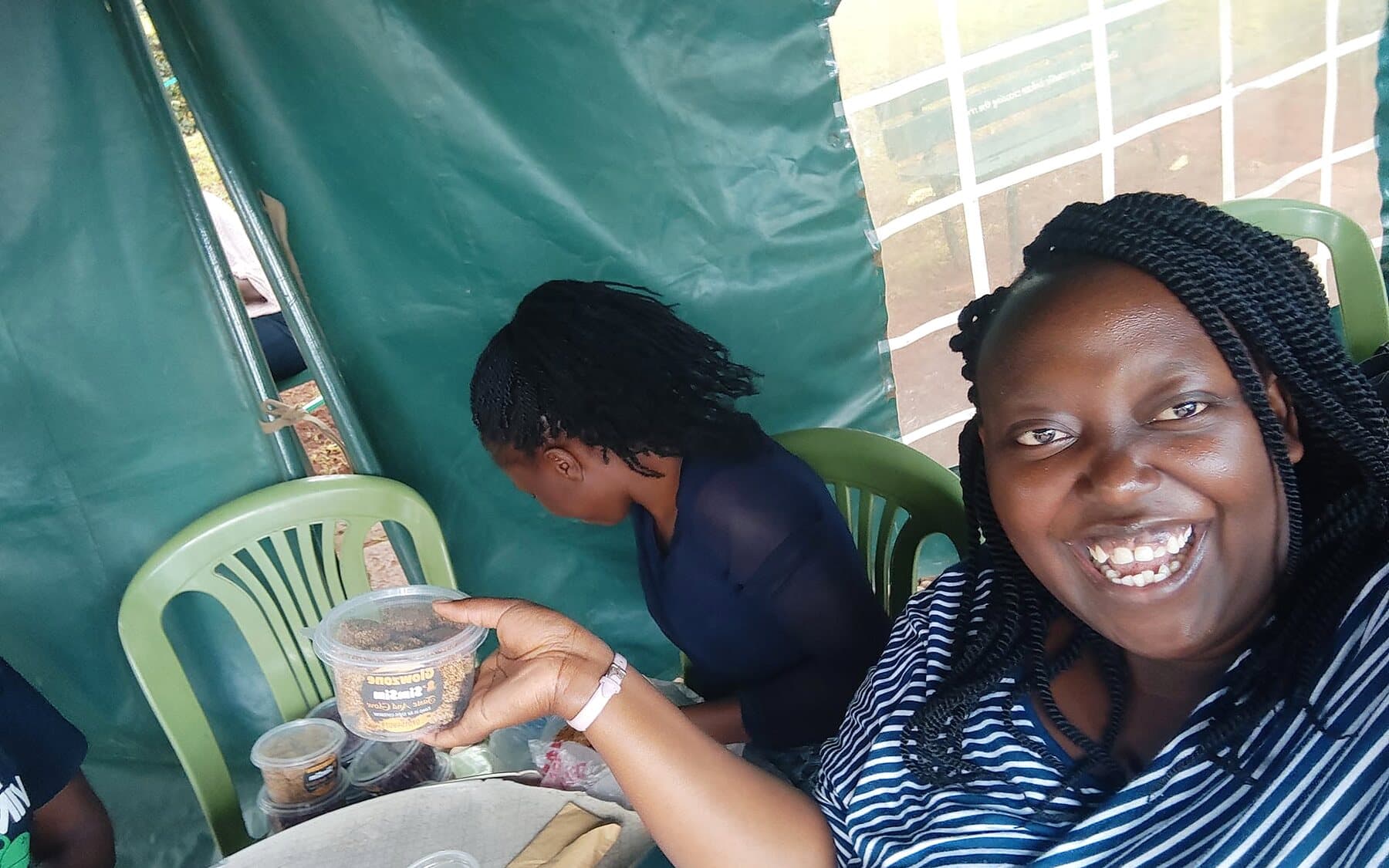 A smiling woman holding a tub of snacks in a market tent